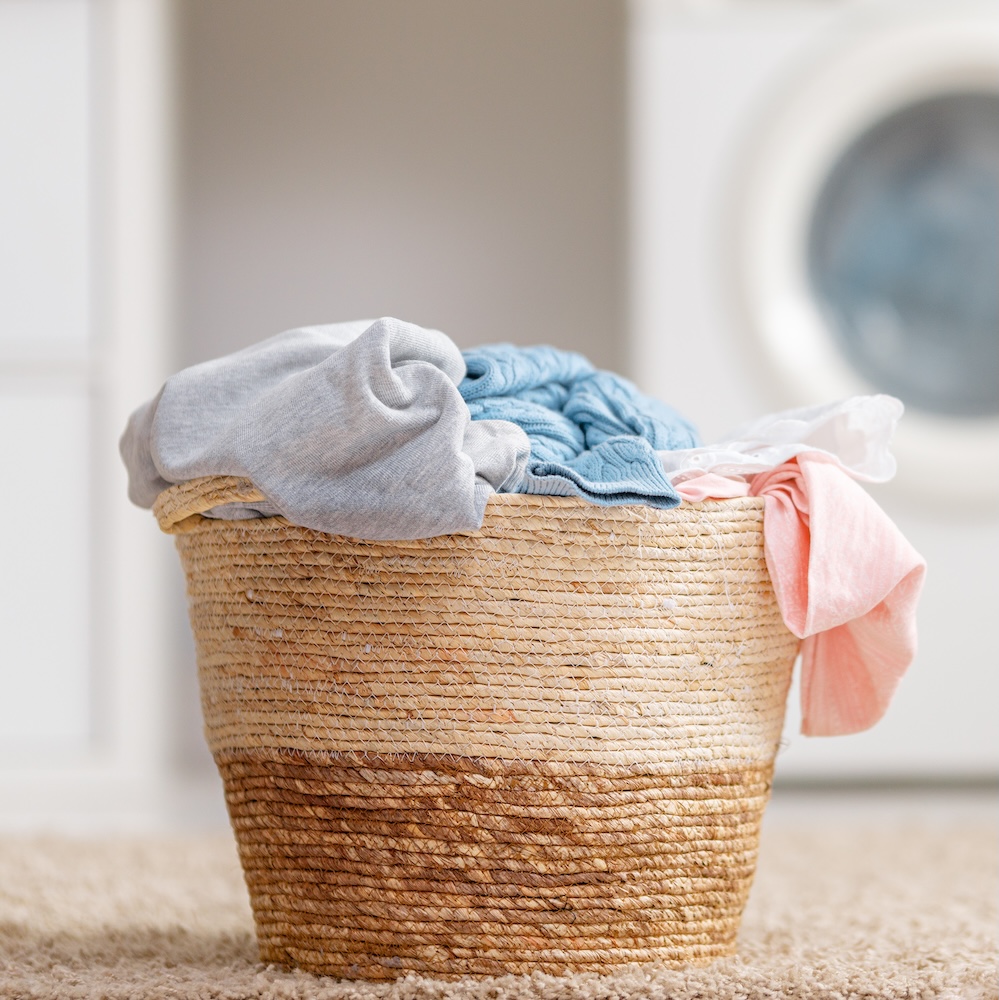 Image of a woven laundry basket with clothes in it. Meant to convey ways to reduce plastic, like by using eco friendly laundry alternatives